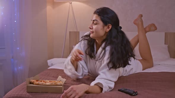Young Woman Eating a Takeaway Pizza Slice at Home While Watching TV