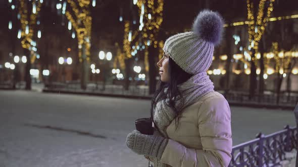 Girl with Coffee Cup in Christmas Evening on Street. alt