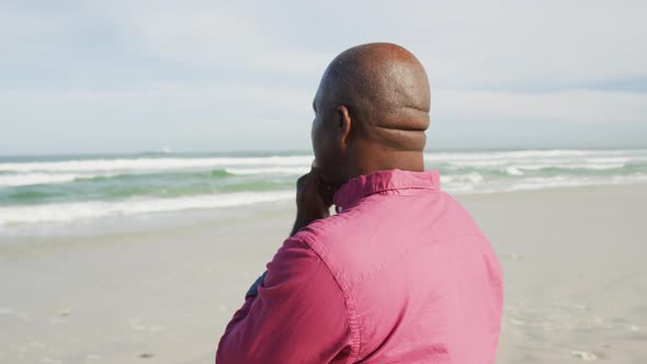 African american man walking on a beach in thought looking at the sea alt