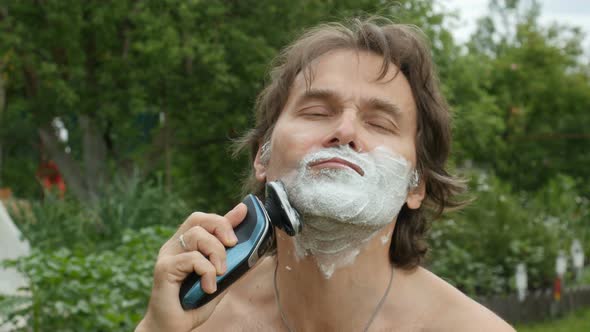 Middle Age Man Shaves His Beard With Foam, Sitting In Yard, Outside. 