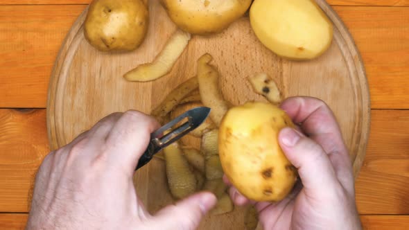 The cook is peeling potatoes. A man peels raw fresh potatoes with a manual potato peeler. Peeled