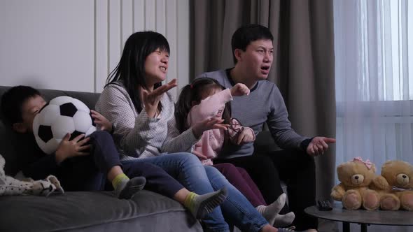 Asian Family Watching Soccer Game in Domestic Room alt