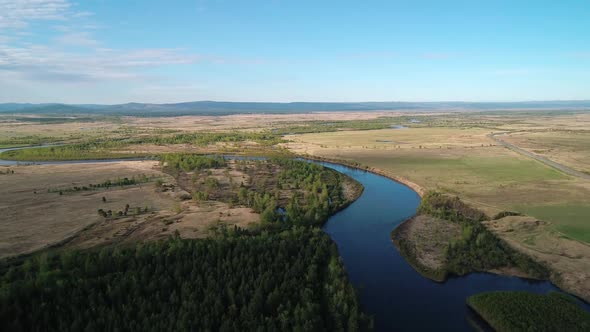 Aerial View of a River Flowing Through Rural Area with Meadows Rare Trees and with the Road on the alt