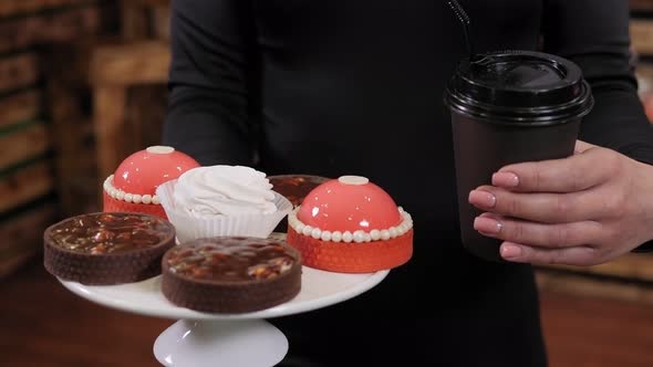 A Beautiful Female Saleswoman Holds a Plate of Cakes and Coffee in Her Hands alt