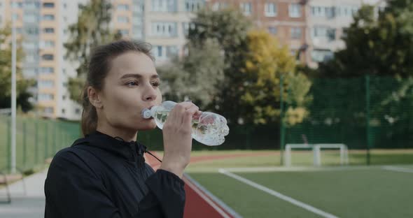 Side View of Positive Young Woman Drinking Water From Bottle and Looking Ahead alt