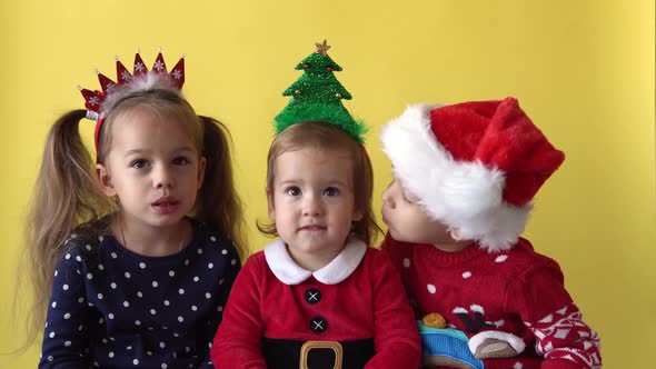 Emotion Cute Happy 3 Siblings Friends Baby Girl And Boy Kissing in Santa Suit Looking On Camera At