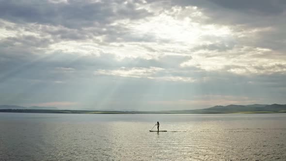 Aerial View of a Woman on a Paddleboard on the Sea in the Mountains at Sunset
