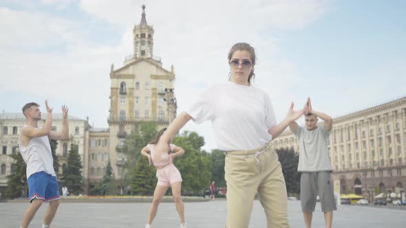 Camera Approaches To Cheerful Young Girl Dancing Robot Dance on Sunny City Square with Group of alt