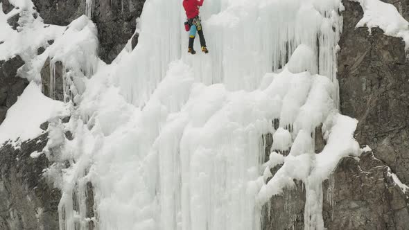 Climber climbs frozen ice sheet cascade with axes aerial 4K alt