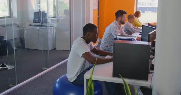 Side view of mixed race business team working on desktop pc at desk in modern office 4k alt