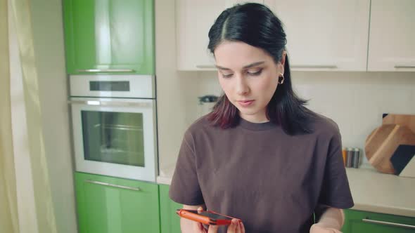 Young Woman in Tshirt Making a Cell Phone Call While Cooking at Home Kitchen