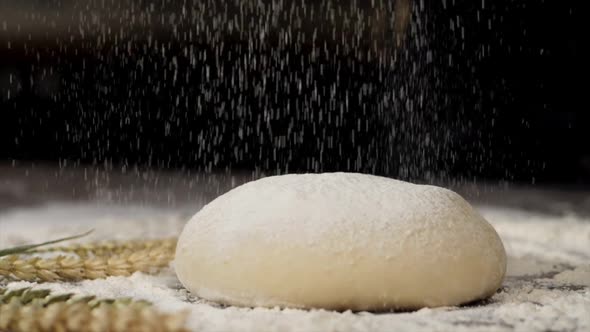 The white flour is falling on the dough in slow motion