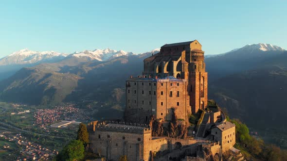 Aerial: drone flying at old medieval abbey perched on mountain top at sunrise, Turin italian Alps alt