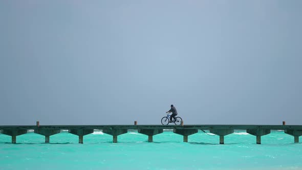 Black Man is Driving Bycicle on the Bridge in the Ocean alt