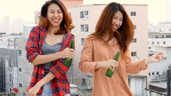 Young Asian woman lesbian couple dancing and clinking bottles of beer party on the rooftop.