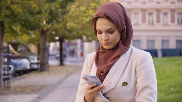 A Young Beautiful Muslim Woman Works on a Smartphone in a Street in an Urban Area  Closeup