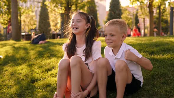 Portrait of a Happy Boy and Girl in the Park on the Grass at Sunset alt