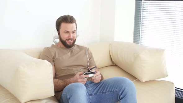Cheerful Man Sitting on Sofa in Living Room Playing Computer Video Game