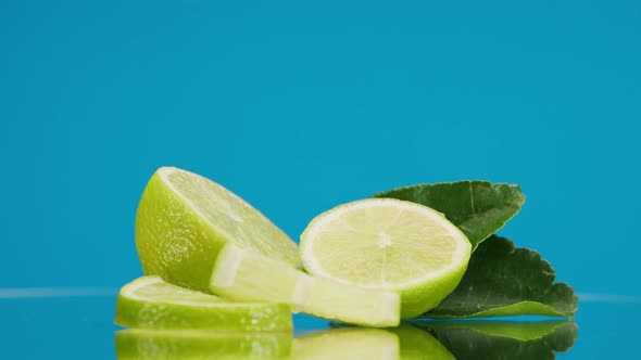 Closeup of Rotating Ripe Limes with Mint Leaves on Blue Background Making a Cocktail of Citrus alt