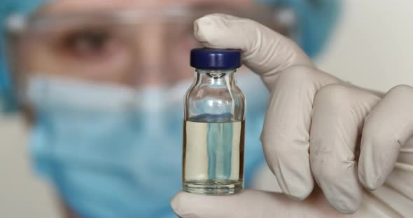 In the laboratory, a Caucasian female scientist in a medical mask analyzes an injection solution in  alt