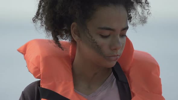 Bruised Female Refugee Holding Life Vest, Looking at Camera, Catastrophe Victim alt