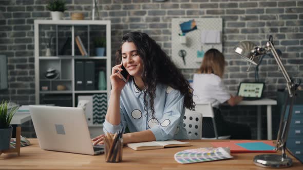 Smiling Woman Talking on Mobile Phone in Office Working with Laptop at Desk alt
