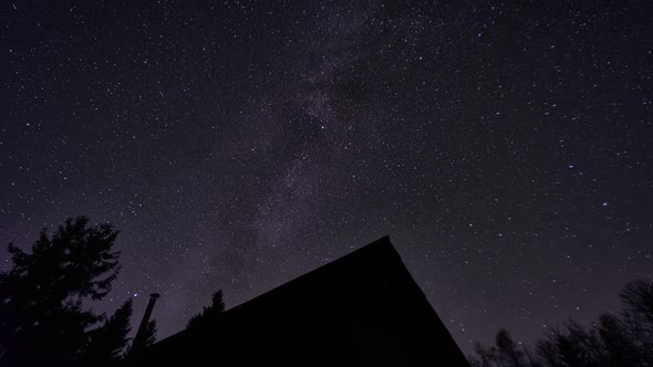 Night sky with the Milky Way. Silhouette of a wooden cottage among the trees. alt