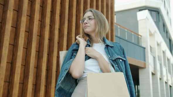 Portrait of Confident Young Lady Standing Outdoors in City with Paperbags on Summer Day alt