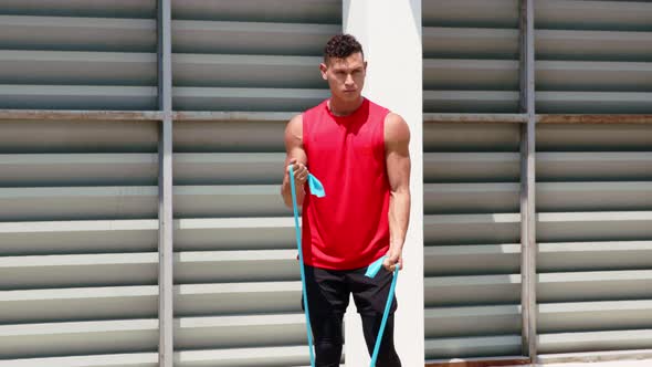 Fit muscular sports man doing bicep curl exercise with resistance band in the open air