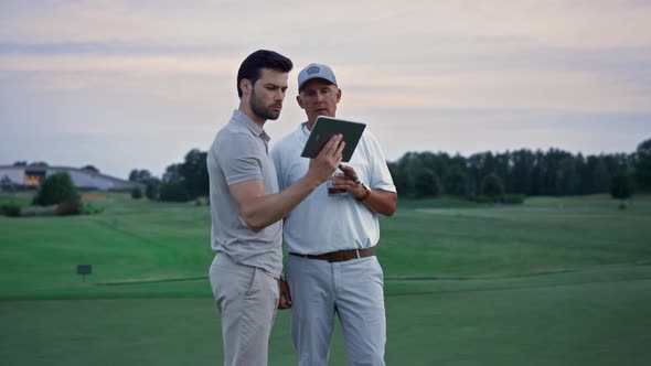 Two Golfers Looking Tablet Watching Tournament Game Video at Golf Course Sunset alt