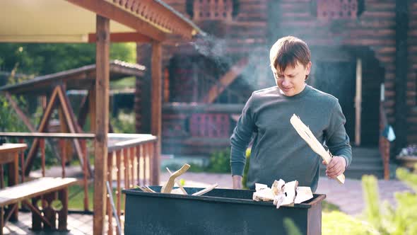 Travelling: Young Guy Is Standing Near the Barbecue, in Which Coals Are Smoking, Against the alt