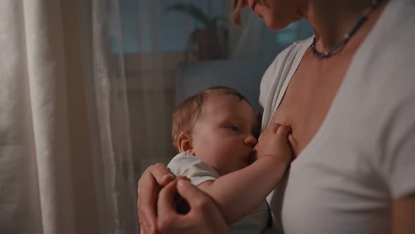 Young Beautiful Mother Breastfeeding Her Newborn Baby Boy at Night Dim Light alt