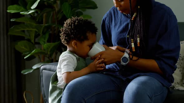 Front view of young black mother feeding milk from glass to her son in a comfortable home 4k alt