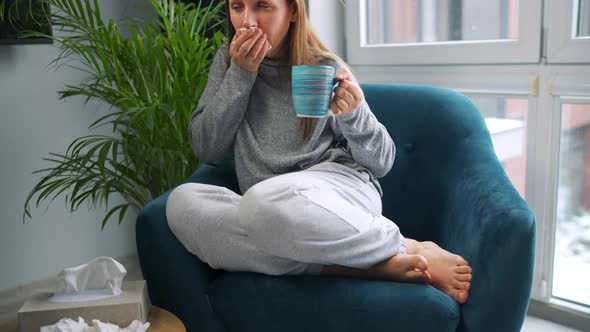 Unhealthy Woman Sits in a Chair Drinks Hot Tea or a Cold Medicine and Sneezes or Blows Her Nose Into alt