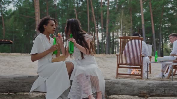 Girls Sharing Secrets and Drinking Sitting at the Campfire in the Woods