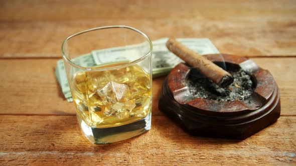 Ashtray, cigar, whisky and US dollars on table 4k alt