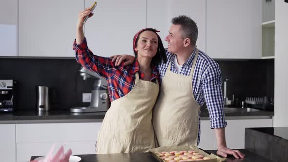 Happy Married Couple in Aprons Takes a Selfie in the Kitchen alt