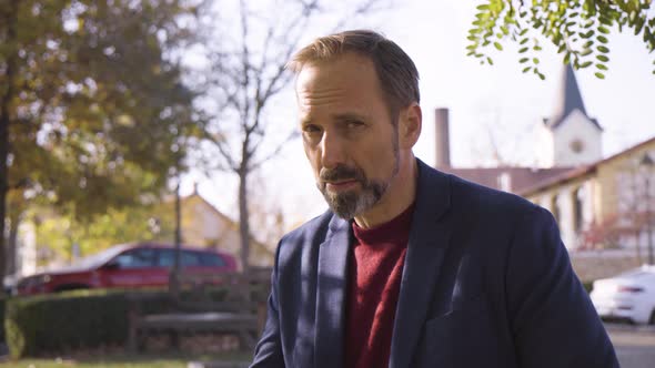 A Middleaged Handsome Caucasian Man Talks to the Camera with a Smile As He Sits on a Bench