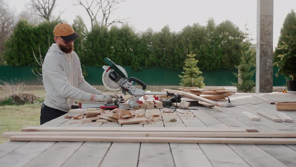 Man Cutting Wood Using Table Saw on Construction Site of a Modern Wooden House alt