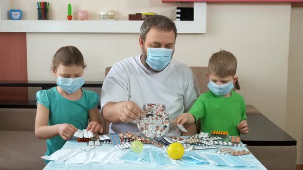 A Father and Children in Medical Masks Lay Out Pills on the Table . Social Distancing and Self