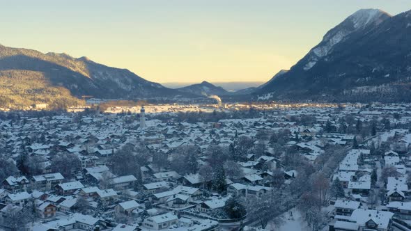 Snowy Garmisch-Partenkirchen town in shadow of mountains, drone shot. alt