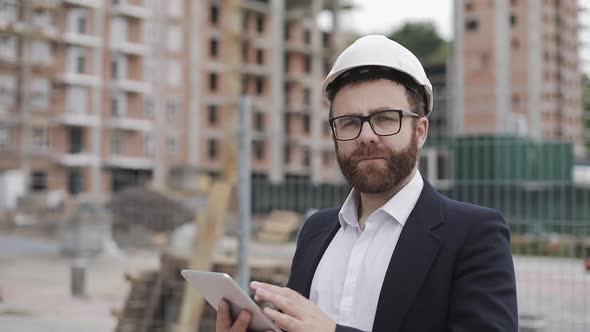 Portrait of Young Businessman with Tablet on Construction Site Looking To Camera Wearing a Safety alt