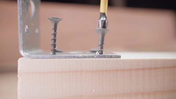The Screwdriver's Cross Bit Twists a Black Selftapping Screw Into a Wooden Block Closeup alt
