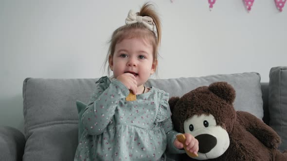Portrait of Charming Female Girl with Cookies in Her Hands Sitting on Sofa in Room