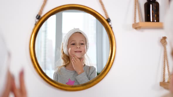 Little Girl Applying Creme on Face in Bathroom alt