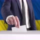 Voting. Man Putting a Ballot into a Voting Box with Ukrainian Flag on Background. - VideoHive Item for Sale