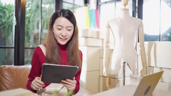 Happy Asian female shop owner checking customer order on digital tablet