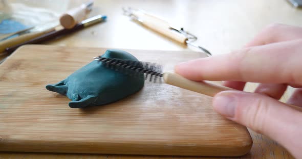 A sculptor or artist carving, sanding and polishing a modeling clay sculpture of a mask figurine wit alt