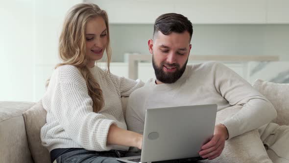Happy Young Couple is Using a Laptop Together Sitting at Home on a Cozy Sofa a Man and a Woman are alt
