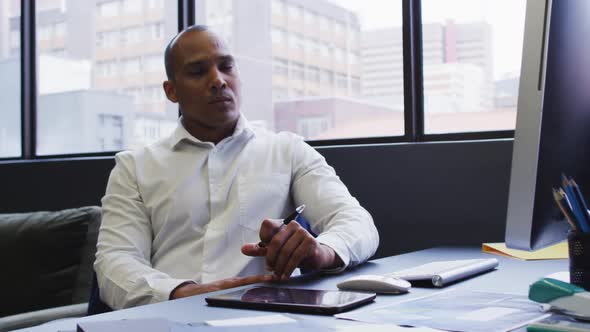 Mixed race businessman sitting using computer rubbing chin in modern office alt